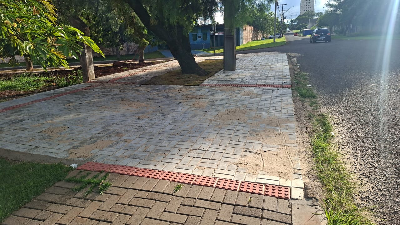 Calçada em paver intertravado com faixa podotátil vermelha em rua arborizada